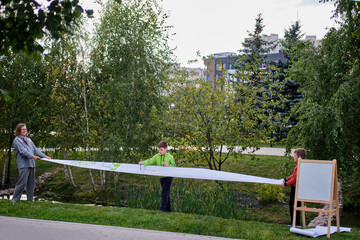 Mother teaches to paint with two boys pupils. Woman teacher artist paints with children on paper nature and trees by the river