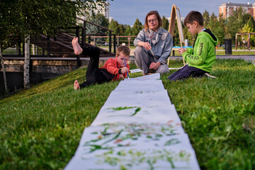 Mother teaches to paint with two boys pupils. Woman teacher artist paints with children on paper nature and trees by the river