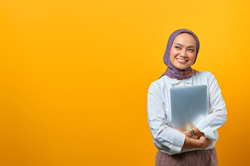 Wall Mural - Portrait of smiling Asian woman bring laptop over yellow background