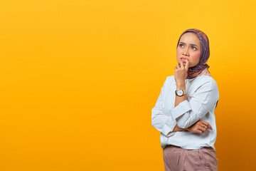 Portrait of thinking Asian woman touching lips and looking at blank space over yellow background