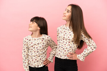 Wall Mural - Little sisters girls isolated on pink background posing with arms at hip and laughing