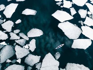 Wall Mural - Kayak sailing between ice floes on the lake. Aerial drone view. Abstract nature background. Baikal lake, Siberia, Russia