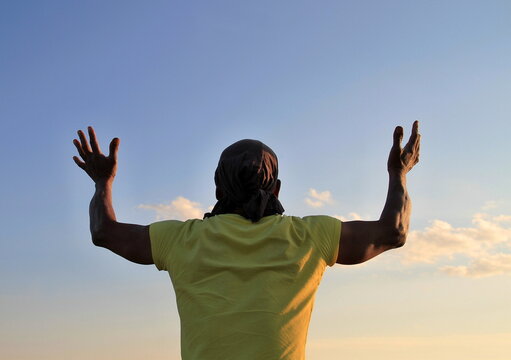 man praying to god with arms outstretched looking up to the sky stock photo