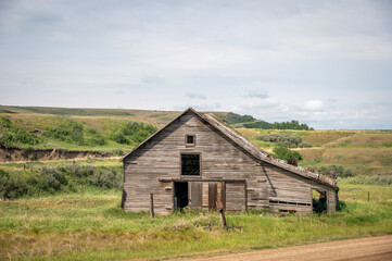 Wall Mural - Horizontal shot of an old destroyed wooden home on a sunny green field under a sky on the horizon