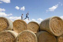 Carefree Brother And Sister Playing On Rolled Hay Bales On Sunny Farm