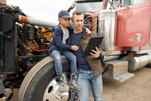 Father And Son Farmers Using Digital Tablet At Semi Truck Engine