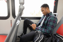 Young Male College Student Using Smart Phone On Public Transit Bus