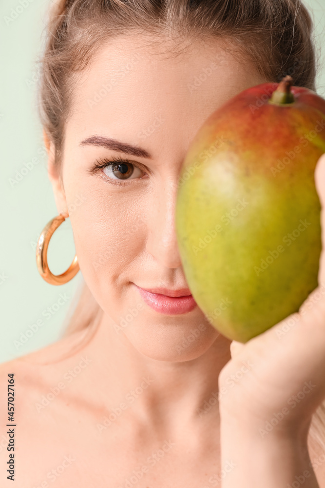 Beautiful woman with fresh mango on color background, closeup