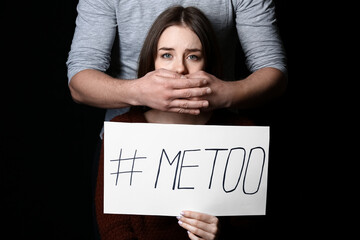 Man and his victim holding paper with hashtag MeToo on dark background