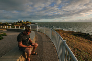 Wall Mural - Digital nomad man working on phone during early morning walk at the Lambert's Beach lookout in Mackay, Queensland Australia