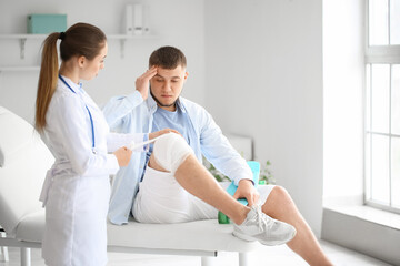 Poster - Doctor applying bandage onto knee of young man in clinic