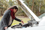 Fototapeta Uliczki - Pregnant young Latina with a concentrated face tries to repair car that broke down in the forest