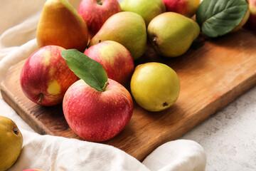 Wooden board with ripe pears and apples on light background