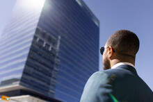 Businessman In Sunglasses Looking Up At Sunny City Highrise Building
