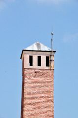 Wall Mural - High brick tower with a lightning rod. Tower with a conical roof against a blue sky background.