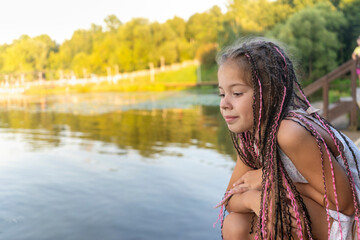 cute little girl with african pigtails on background of lake and beach in close - up looks mysteriou