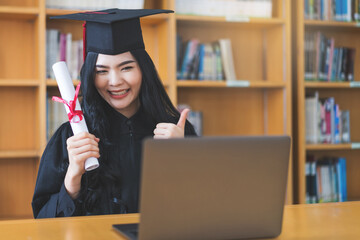 Wall Mural - University graduate in graduation gown and mortarboard celebrates in a virtual graduation ceremony. Happy female student on her graduation day at home. Concept of online education