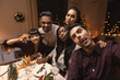 holidays, friendship and celebration concept - multiethnic group of happy friends having christmas dinner at home and taking selfie