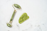 Fototapeta Mapy - Jade roller and gua sha stone massager at white bath towel. Anti aging therapy. Top view with copy space..