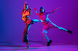 Two dancers, young man and woman dancing hip-hop in casual sports youth clothes on gradient purple pink background at dance hall in neon light.