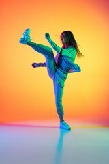 Wall Mural - Portrait of young sportive girl dancing hip-hop in stylish clothes on colorful background at dance hall in neon light. Youth culture, movement, style and fashion, action.