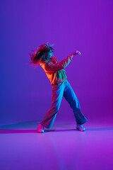 Wall Mural - Stylish sportive girl dancing hip-hop in stylish clothes on colorful background at dance hall in neon light. Youth culture, movement, style and fashion, action.