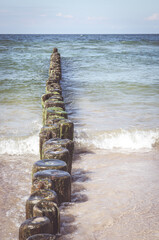 Poster - Vertical shot of the wooden breakwater in the wavy water under a blue clear sky