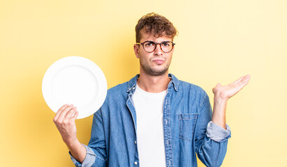 Wall Mural - young handsome man feeling puzzled and confused and doubting. empty dish concept