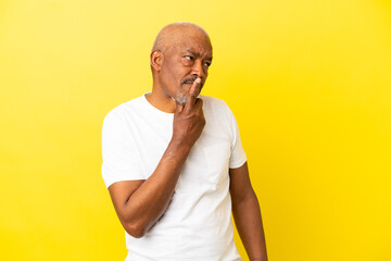 Cuban Senior isolated on yellow background having doubts and with confuse face expression