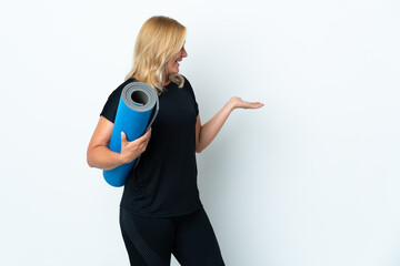 Wall Mural - Middle age woman going to yoga classes while holding a mat isolated on white background with surprise facial expression