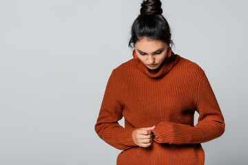 Wall Mural - young woman in knitted sweater looking down isolated on grey