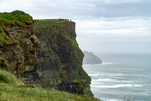 Breathtaking View Of High Green Cliff By Wavy Sea Under Cloudy Sky