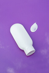 Wall Mural - Plastic white tube for cream or lotion and the appearance of the texture of the cream on a purple background . Skincare sunscreen cosmetic in top view. Beauty concept for face body care