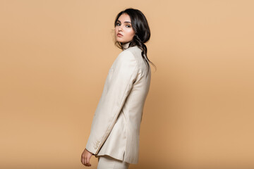 Sticker - young pretty woman in turtleneck and suit looking at camera isolated on beige