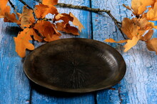 Dry Yellow Oak Leaves On A Black Clay Plate On An Old Blue Wooden Board Background. Autumn Concept