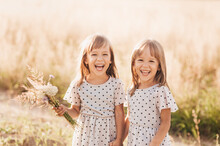 Two Little Happy Identical Twin Girls Playing Together In Nature In Summer. Girls Friendship And Youth Concept. Active Children's Lifestyle.