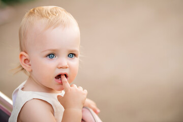 portrait of blue-eyed baby sucking finger in her mouth, two first teeth are visible.