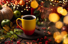 Red And Yellow Mug With Mulled Wine. Fruits And Spices Are All Around On A Wooden Table. Yellow Lights Of Garlands Are Burning Behind