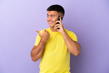 Poster - Young handsome man using mobile phone over isolated purple background pointing to the side to present a product