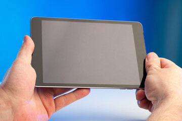 Poster - Tablet computer in the hands of a man. Tablet computer with screen off. Man shows a tablet screen. Electronic gadget on a blue background. Concept - selling gadgets. Sale of pocket computers