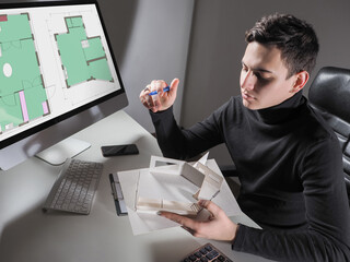 Poster - Architect student while studying. He makes a volumetric layout of house. Architect student next to computer. Concept - training as an architect. Architectural drawings in student computer