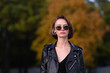 © deine_liebe - Portrait of a girl with short hair in a leather jacket in the autumn forest. Young hipster or rocker woman with big earrings in her ears posing on the street.