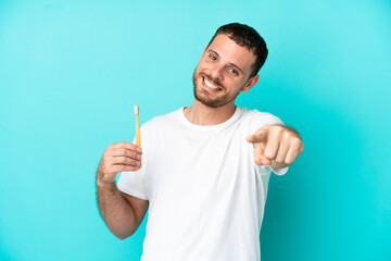 Young Brazilian man brushing teeth isolated on blue background pointing front with happy expression