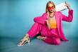 © Victoria Fox - Fashion portrait of elegant confdent woman wearing trendy summer pink fuchsia color suit, strappy sandals, orange sunglasses, holding white quilted faux leather bag, posing in studio. Copy cpace