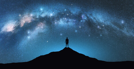 Wall Mural - milky way arch and man on the mountain peak at starry night. silhouette of alone guy, blue sky with 