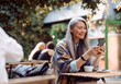 © Yaroslav Astakhov - Happy mature Asian woman surfs internet on mobile phone sitting at small table on outdoors cafe terrace on autumn day