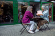© Yaroslav Astakhov - Excited senior Asian woman opens gift presented by best friend sitting at small table on outdoors cafe terrace on autumn day