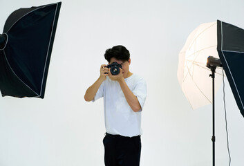 Young asian photographer looks through the viewfinder while shooting with the camera. Working atmosphere in the photo studio.