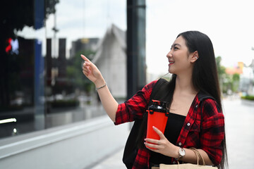 Cheerful Asian woman holding coffee cup and shopping bags walking in the city.