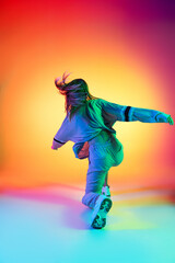 Wall Mural - Young sportive girl dancing hip-hop in stylish clothes on colorful background at dance hall in neon light. Youth culture, movement, style and fashion, action.